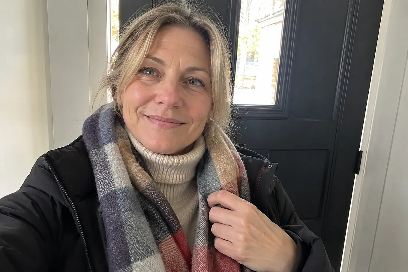 A turtleneck beneath a jacket and scarf fills the frame on a woman over 50 returning home on a cold day, with no writing visible.