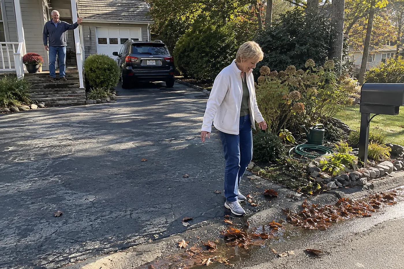 Older woman looking at wet leaves on her driveway before walking to the mailbox.