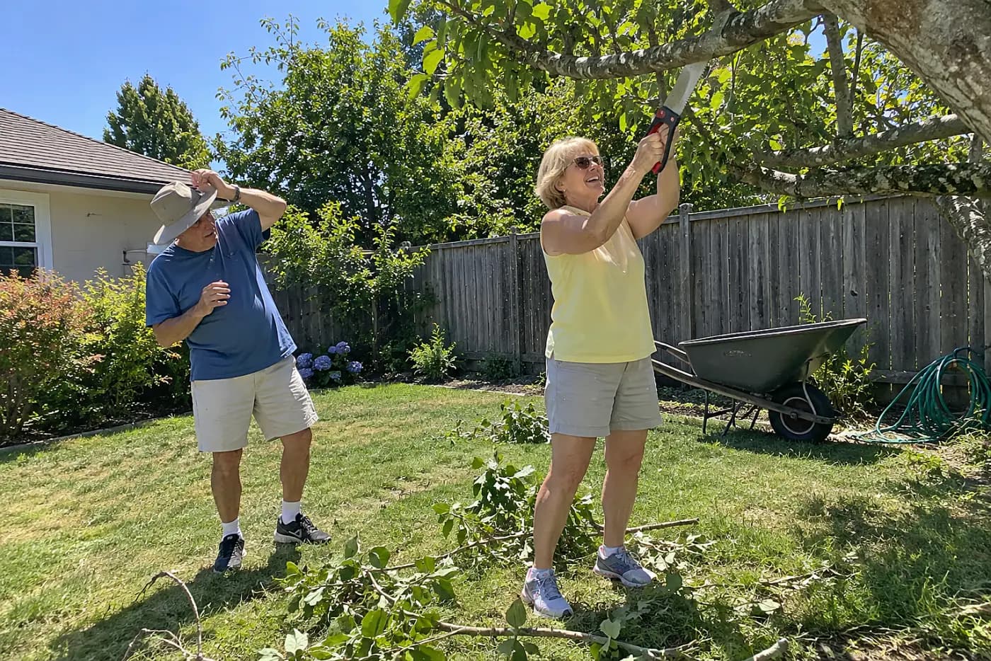 Woman making an underside cut on a large branch in her backyard.