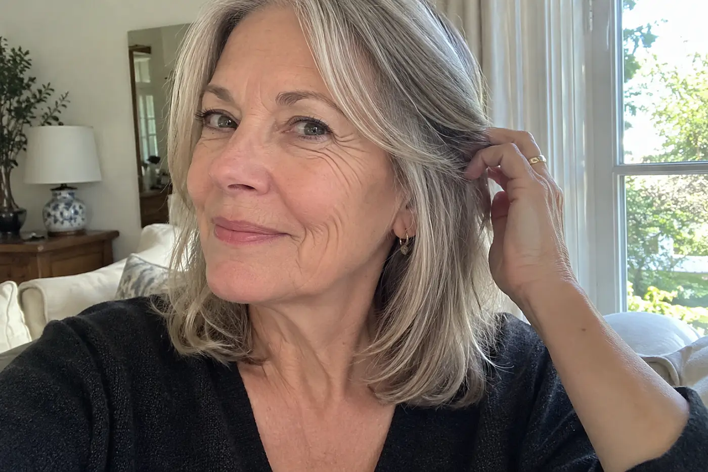 A lob with face-framing pieces sits at the center of a close portrait of a woman in her sixties at home in daylight, with no writing visible.