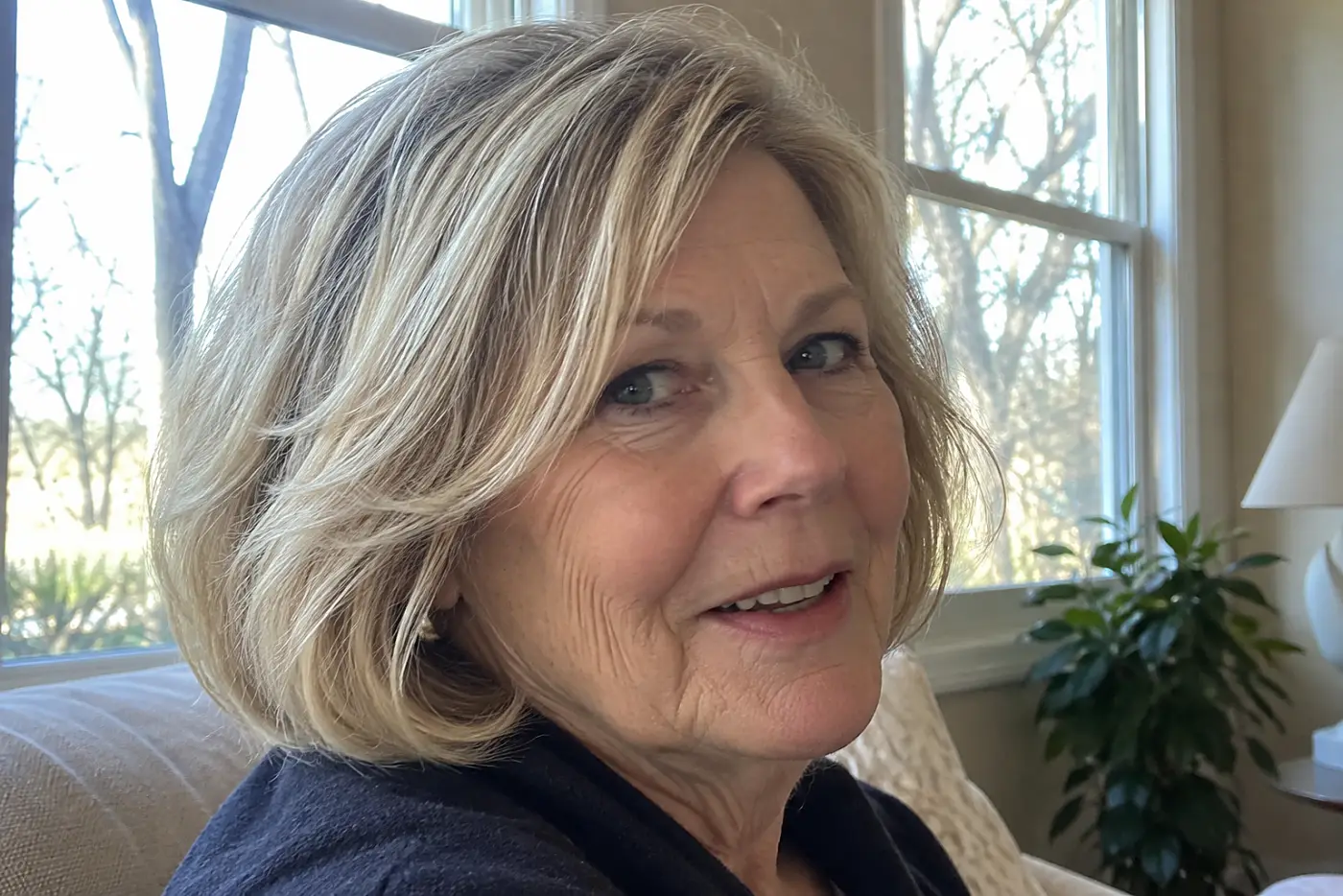 A rounded chin-length bob fills the center of a three-quarter view of a woman in her sixties seated near a window, with no writing visible.