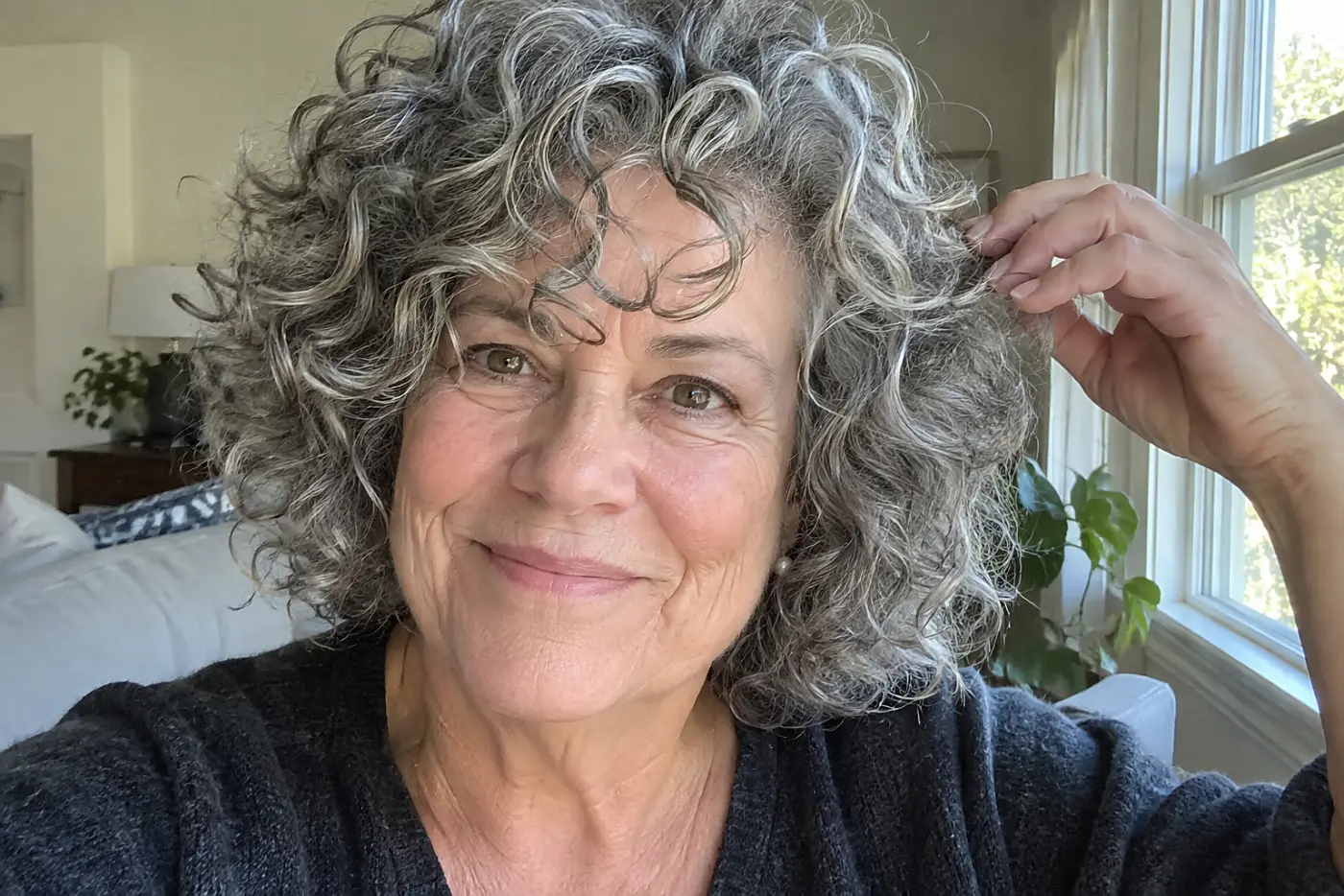 A curly cut with forehead curls fills the center of a close portrait of a woman in her sixties at home in daylight, with no writing visible.