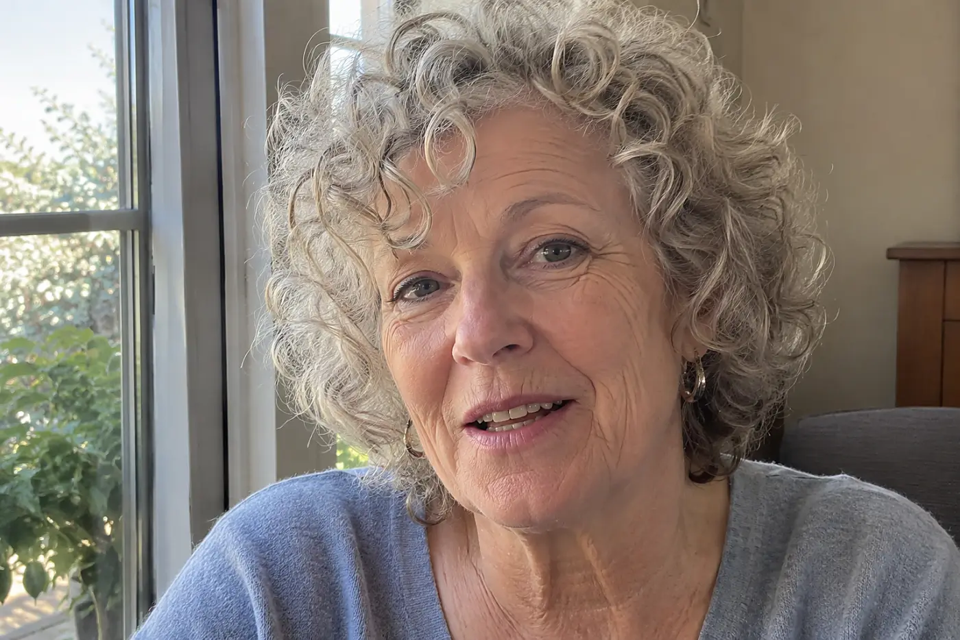 A curly bob with a rounded shape is centered on a woman in her sixties seated near a bright window, with no writing visible.