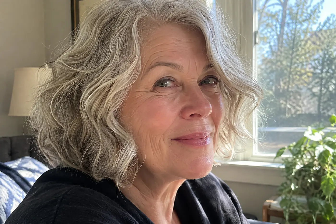 A wavy bob above the shoulders fills the center of a portrait of a woman in her sixties turning her head in daylight, with no writing visible.