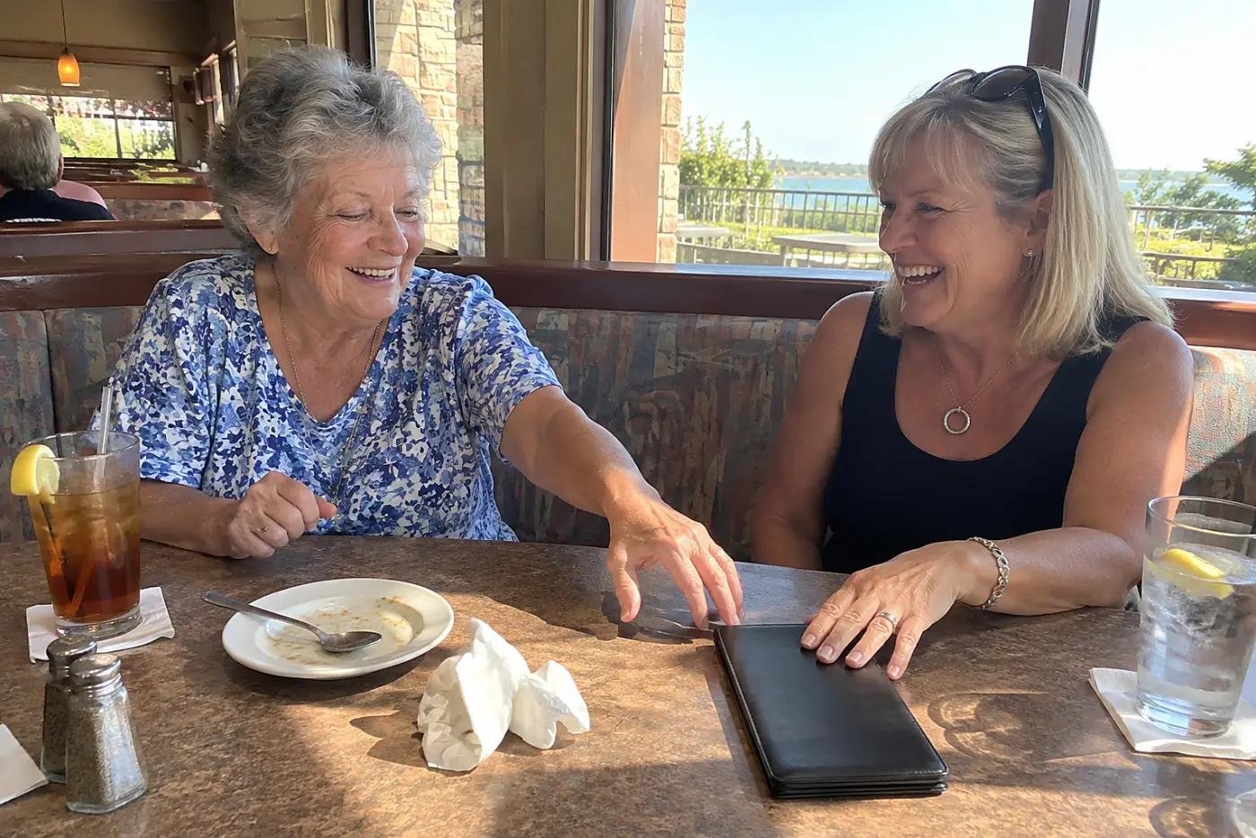 Older woman reaching for a dinner check at a restaurant table with her daughter.