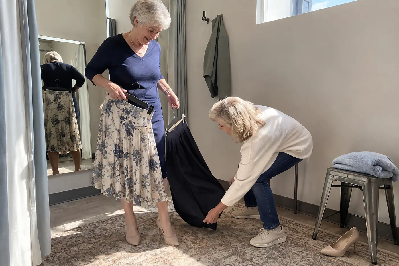 Older woman comparing two skirt hems while wearing heels in a fitting room.