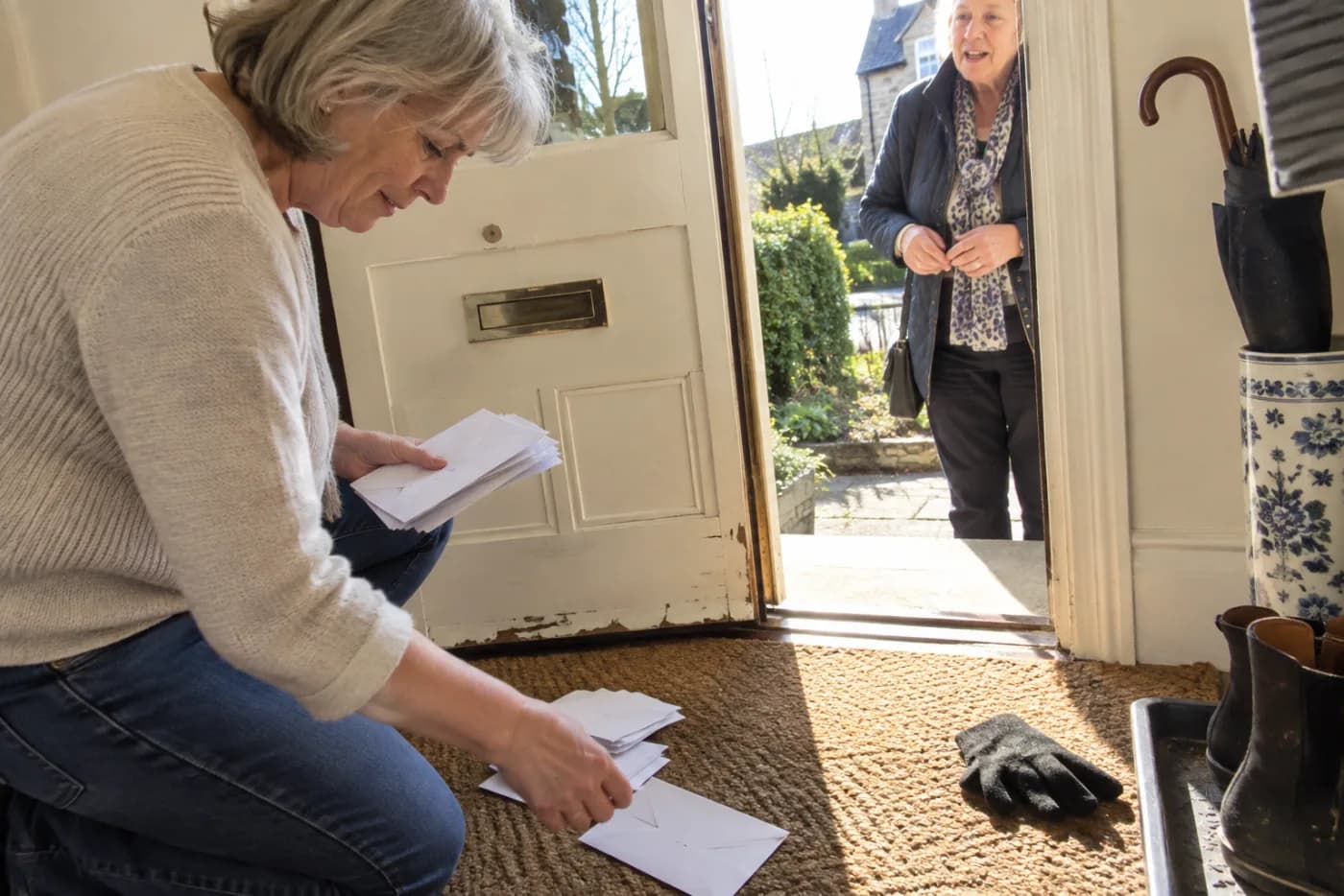 Older woman sorting envelopes beside the mail slot in her front door.
