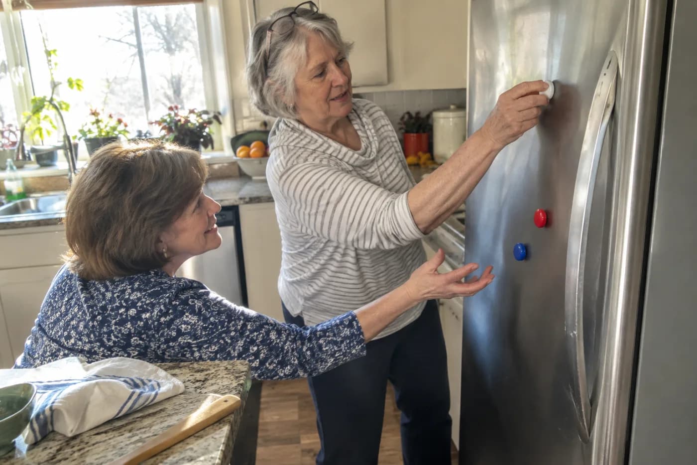 Older woman removing magnets from a refrigerator in a kitchen.