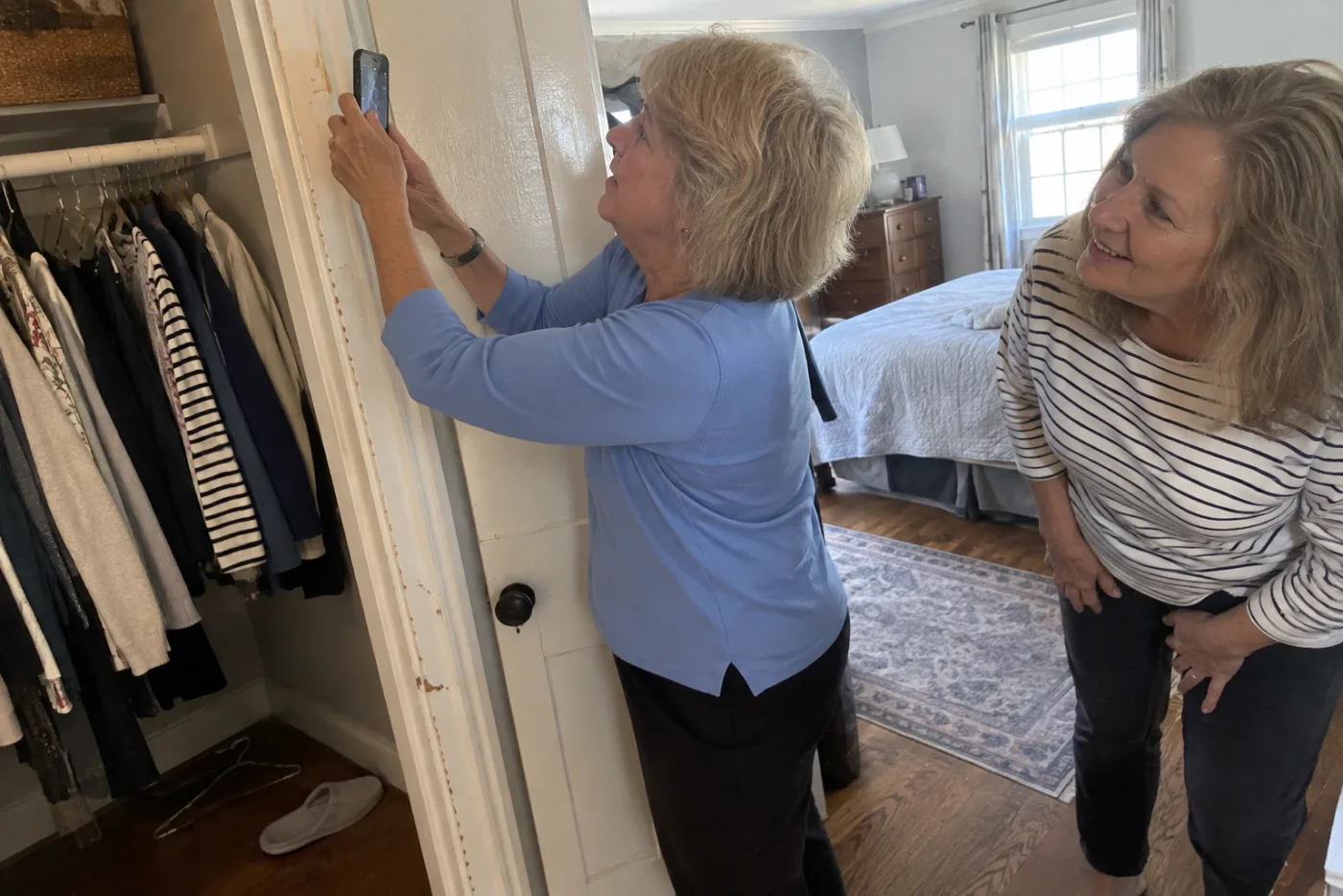 Older woman photographing pencil height marks inside a bedroom closet.