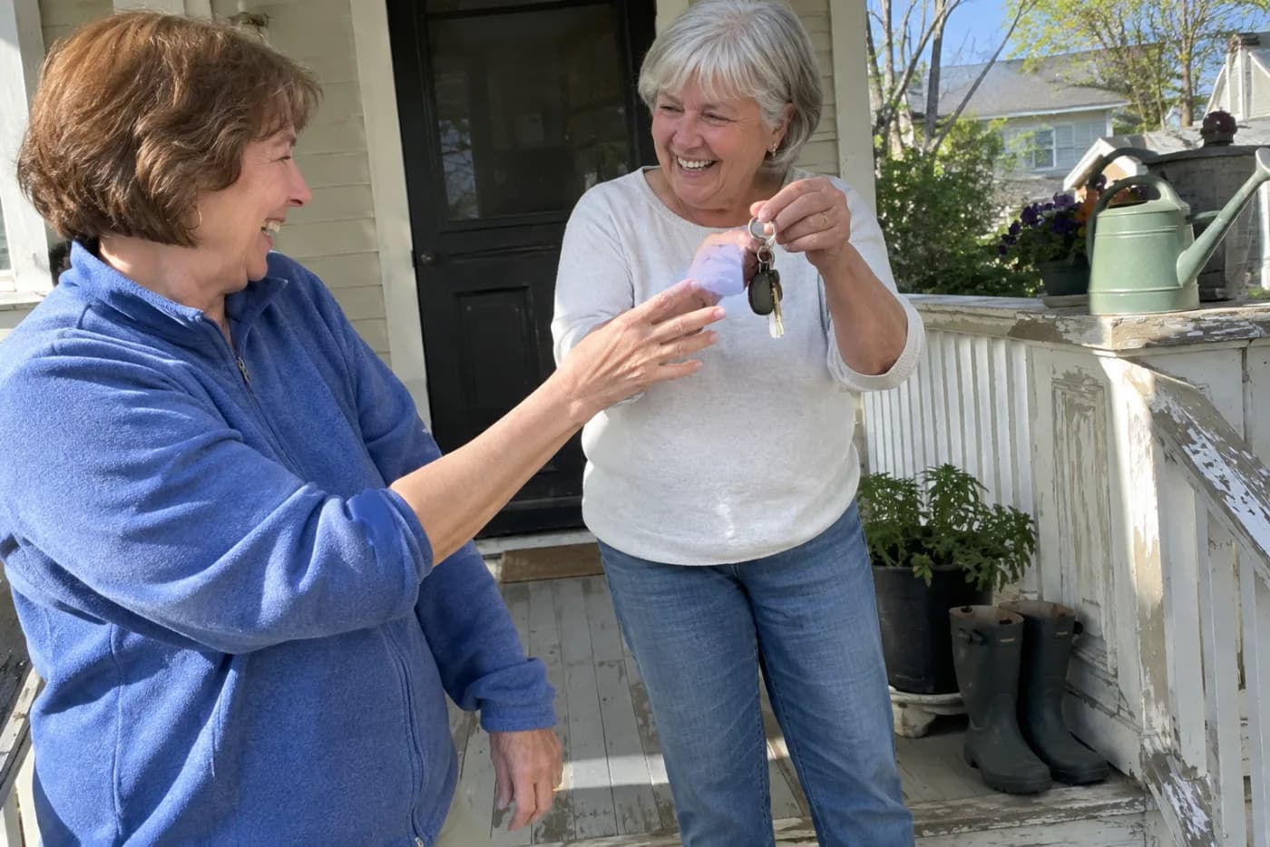 Older woman accepting a spare key from a neighbor on the neighbor’s porch.