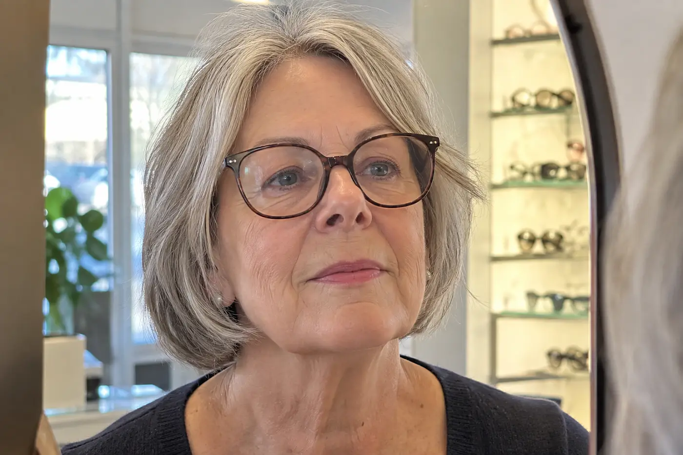 A woman’s pupils sit high and inward in the glasses at the middle of a straight-on view of her at an optical shop mirror.