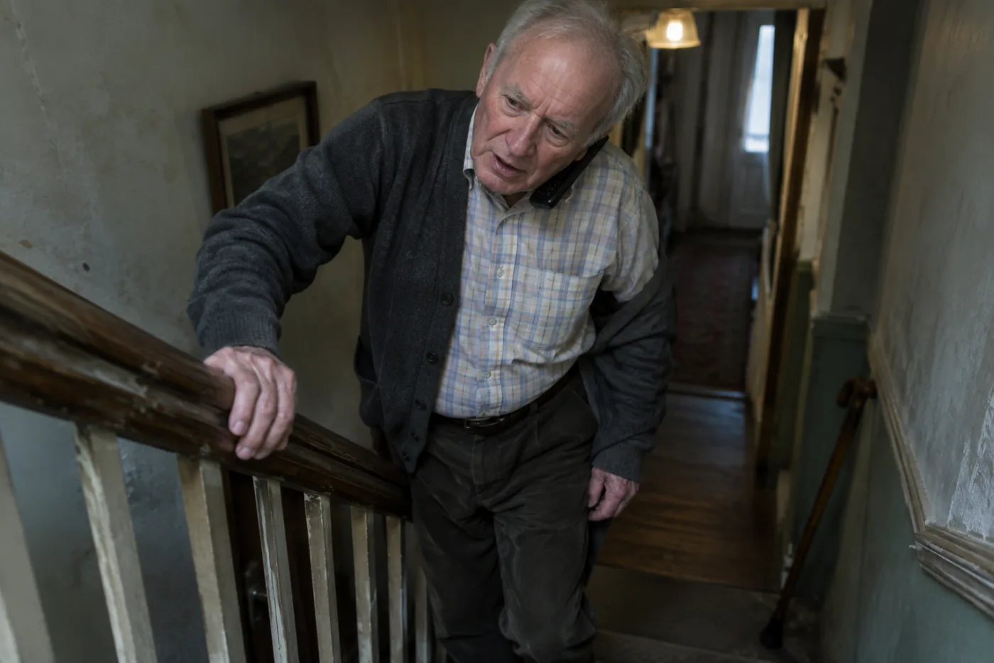 Elderly man steadying himself on stairs while quickly answering a phone call