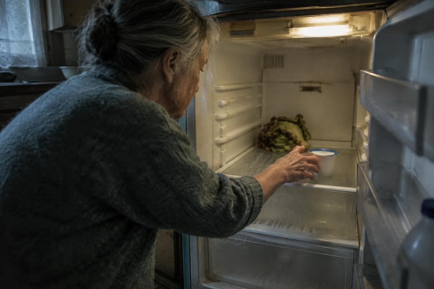 Woman reaching into a nearly empty refrigerator with wilted produce visible