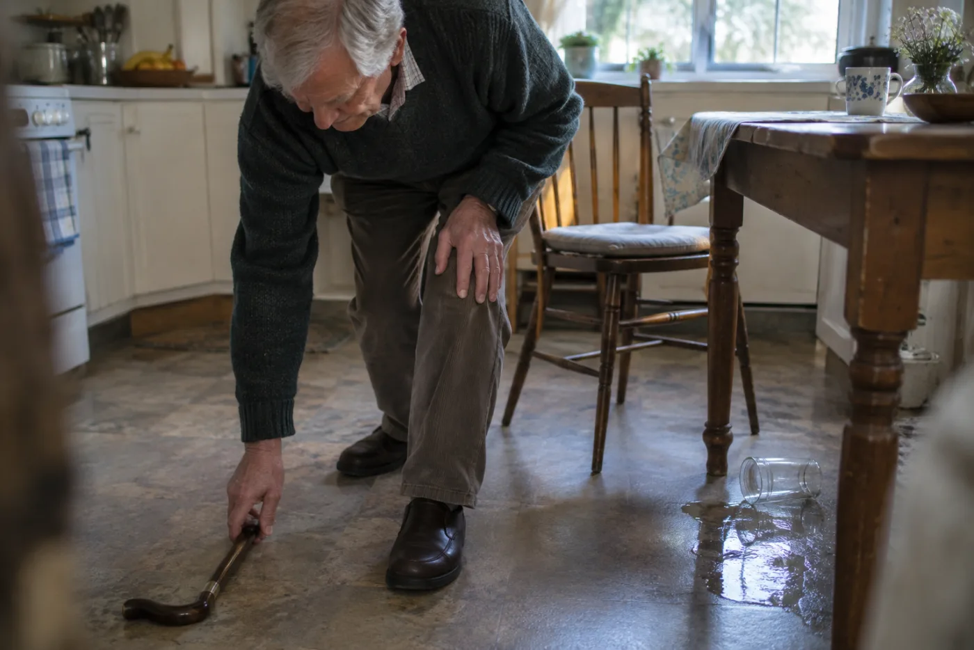 Man brushing off his knee and picking up a dropped cane in the kitchen