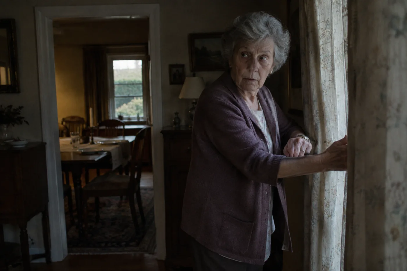 Woman closing a curtain and checking her watch as an unexpected car arrives