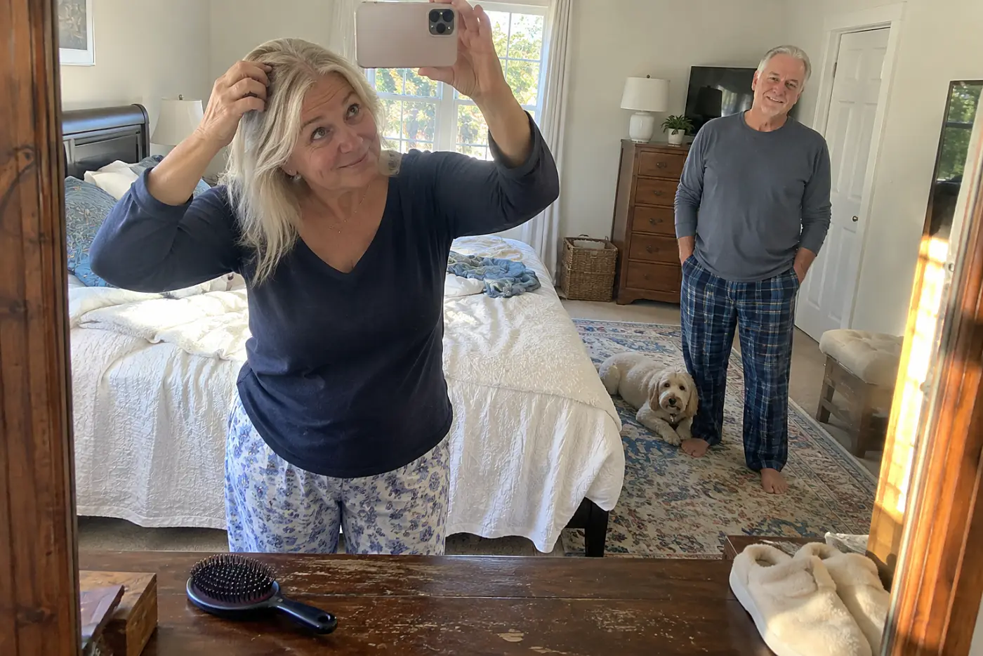 Older woman photographing her hair part in a bedroom mirror.