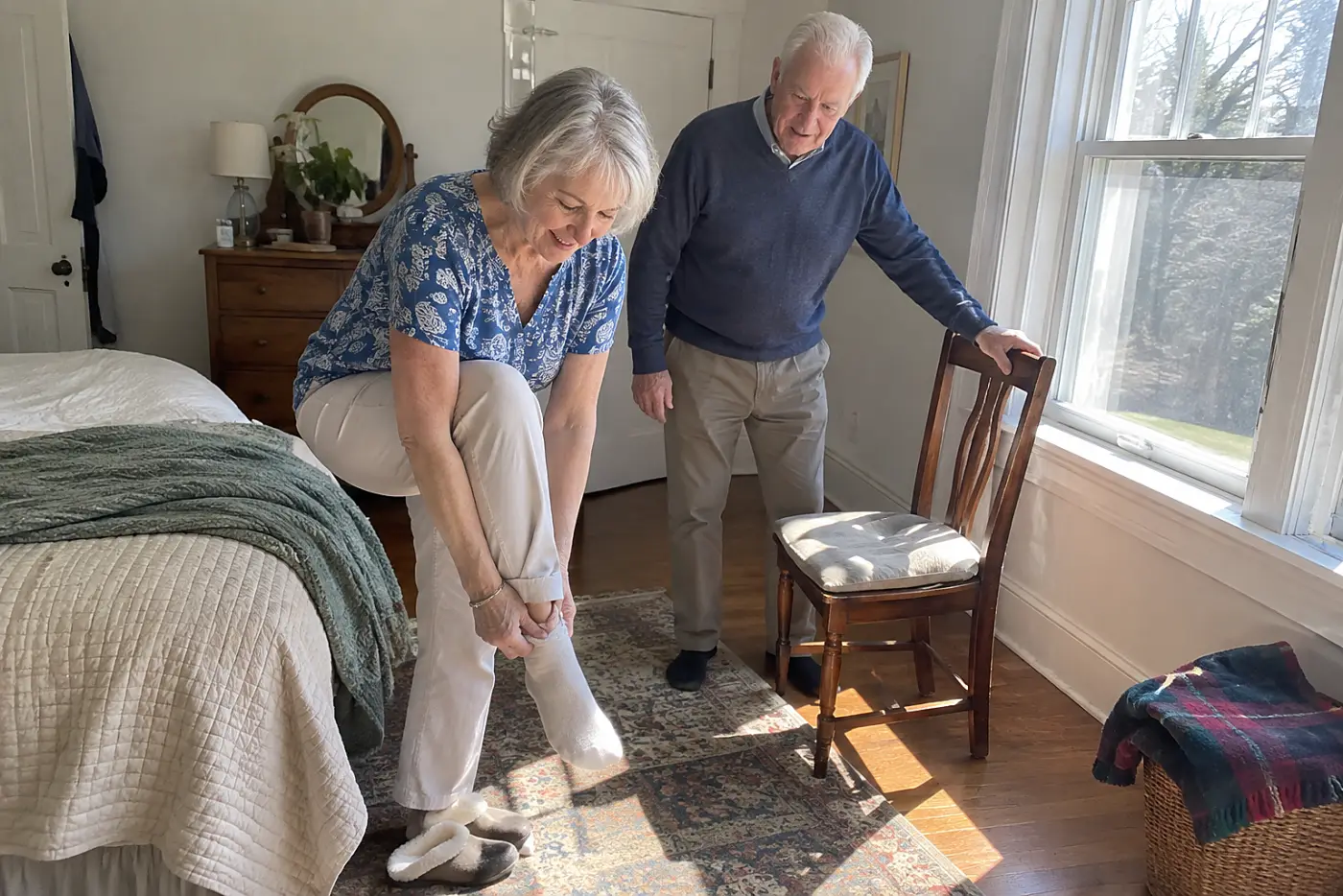 Older woman examining her shin beside her bedroom window.