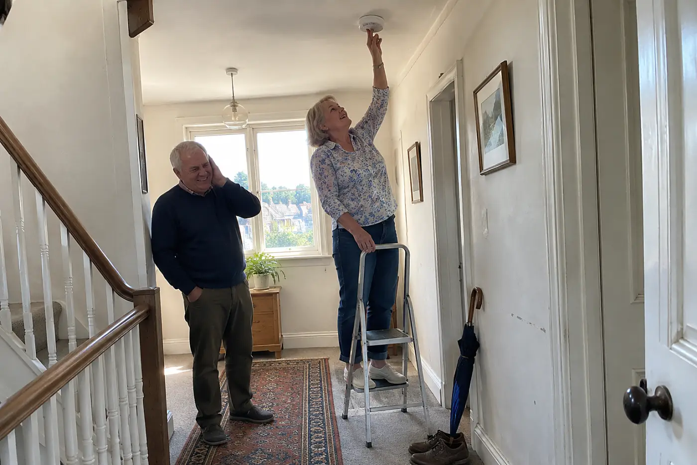 Older woman pressing a smoke alarm test button in her hallway.