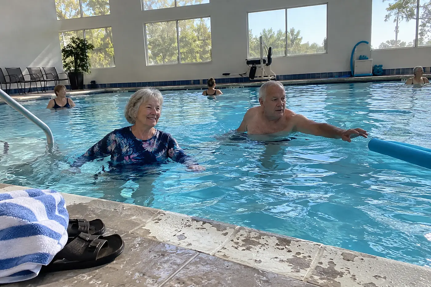 Older woman walking through chest-deep water in a community pool.