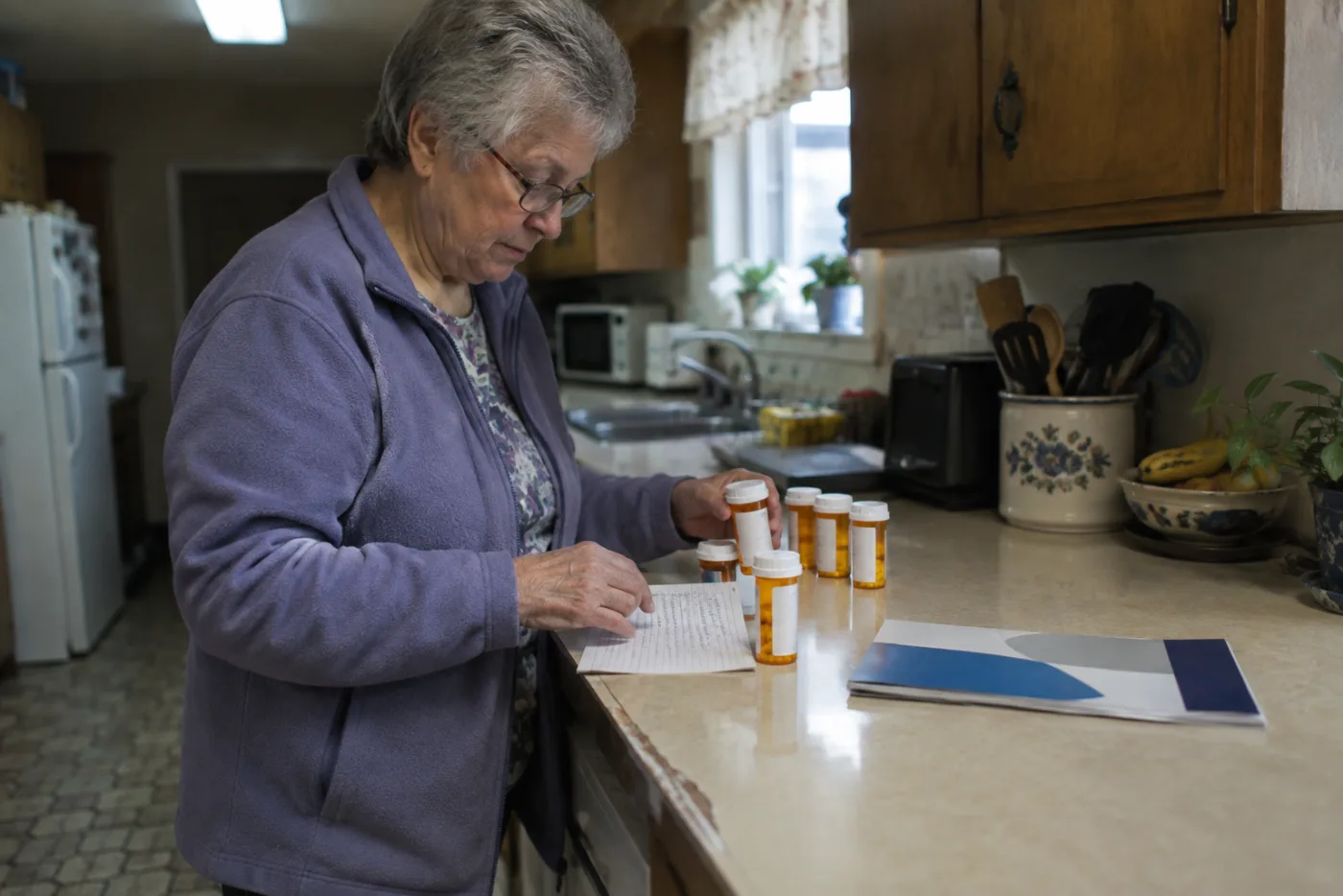 Woman lining up pill bottles beside an insurance enrollment booklet on a counter