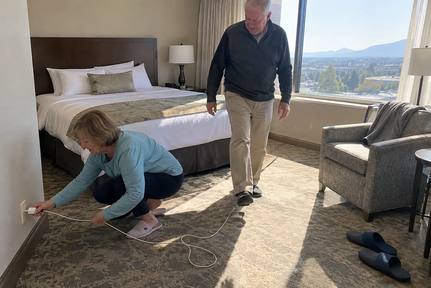 Older woman plugging a long charging cable into a hotel room outlet.