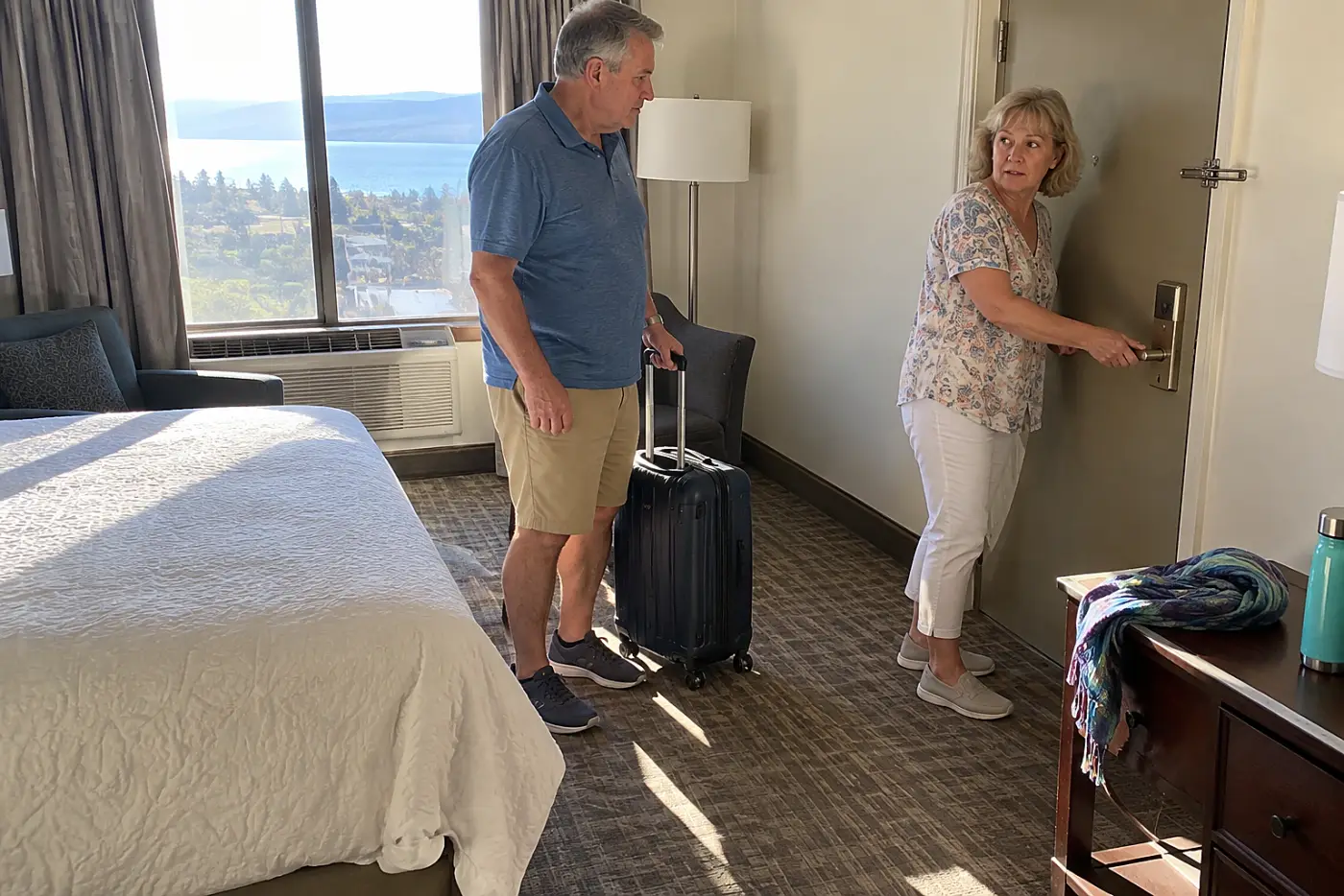 Older woman checking a hotel room door lock with her suitcase still packed.