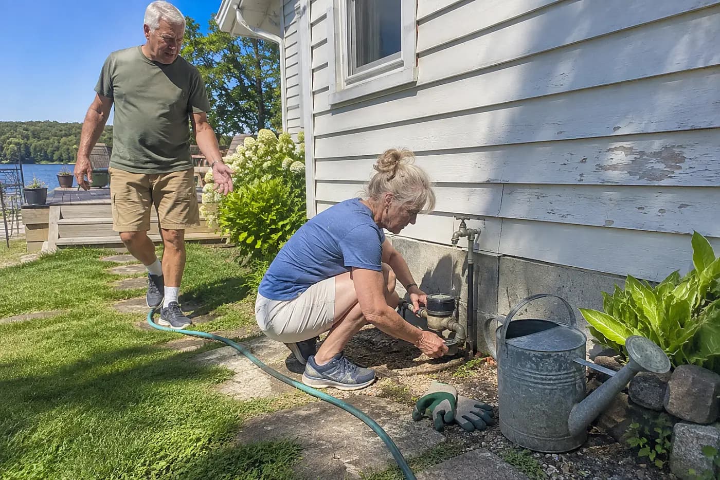 Older woman reading a water meter beside her house.