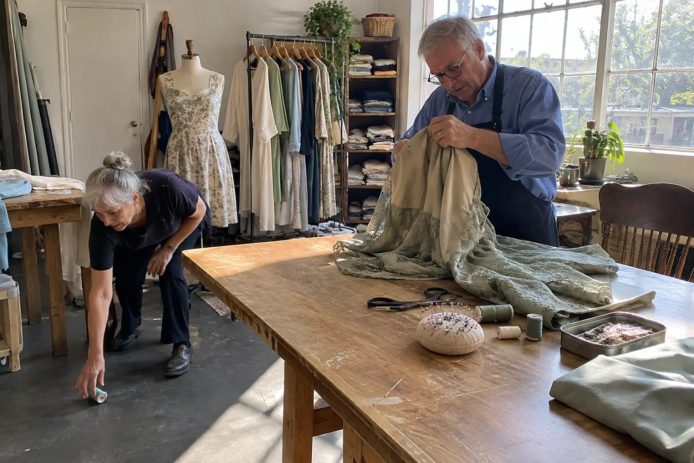 Tailor examining old stitch holes inside a dress at a worktable.