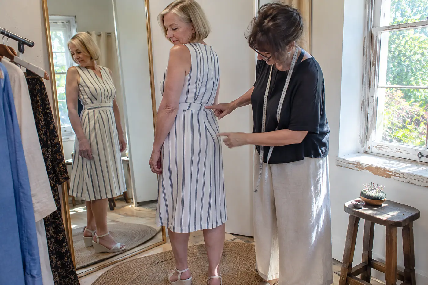 Woman comparing the stripes at a dress seam beside a fitting-room mirror.