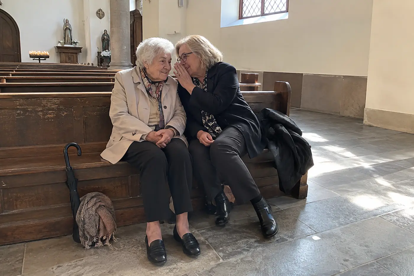 Woman sitting beside her friend in the back row of a chapel.