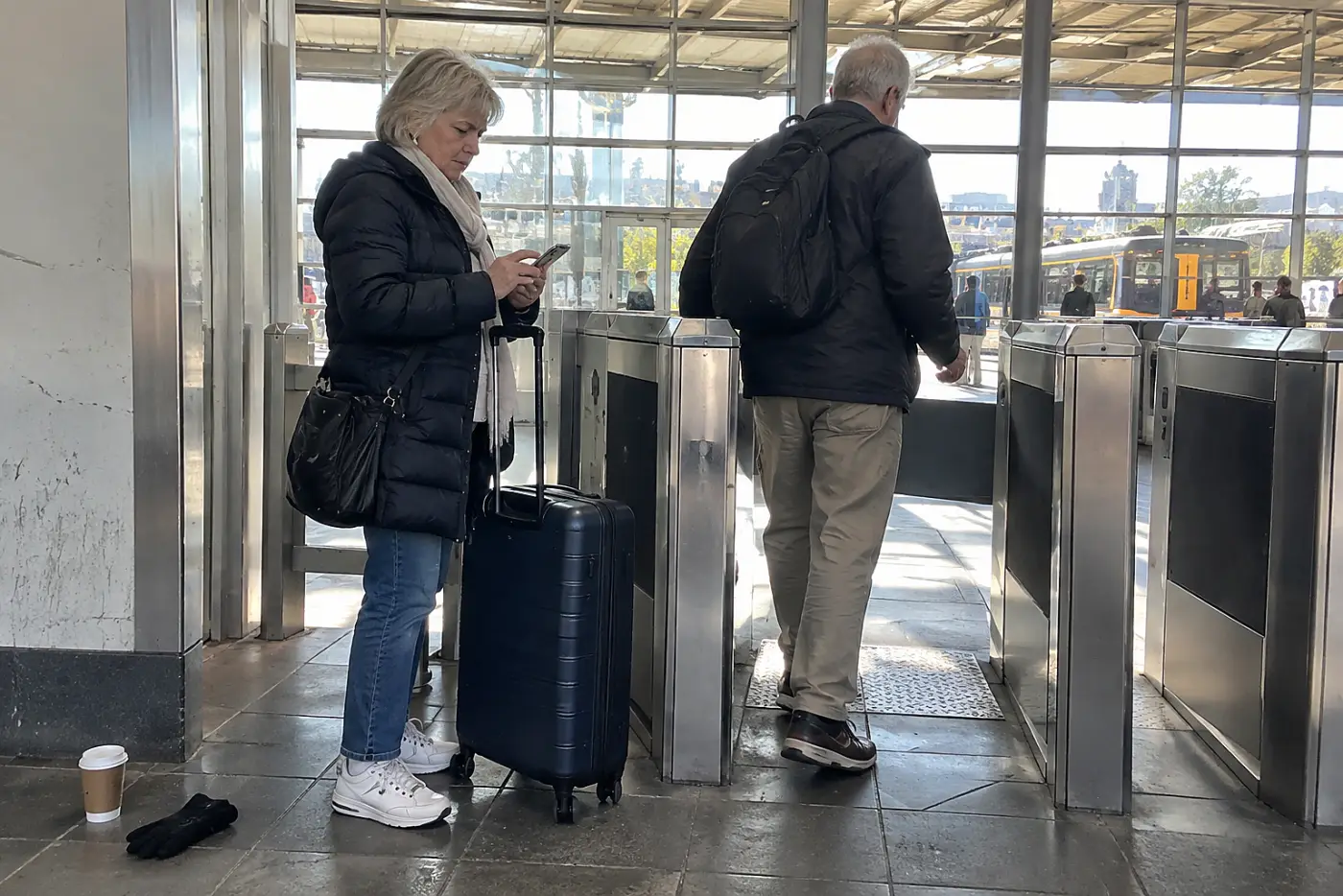 Woman opening a saved ticket on her phone beside a station gate.