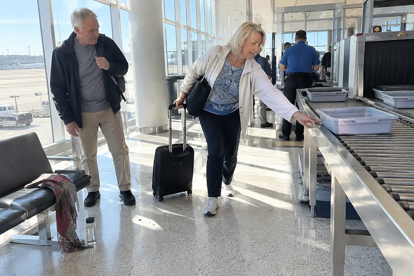Older woman pulling a carry-on through an airport security area.