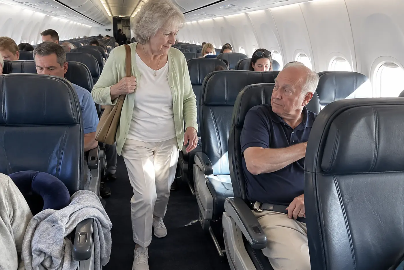Older woman walking down an airplane aisle during a flight.
