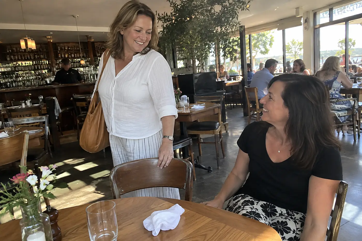 Woman talking with a friend while standing beside a restaurant table.