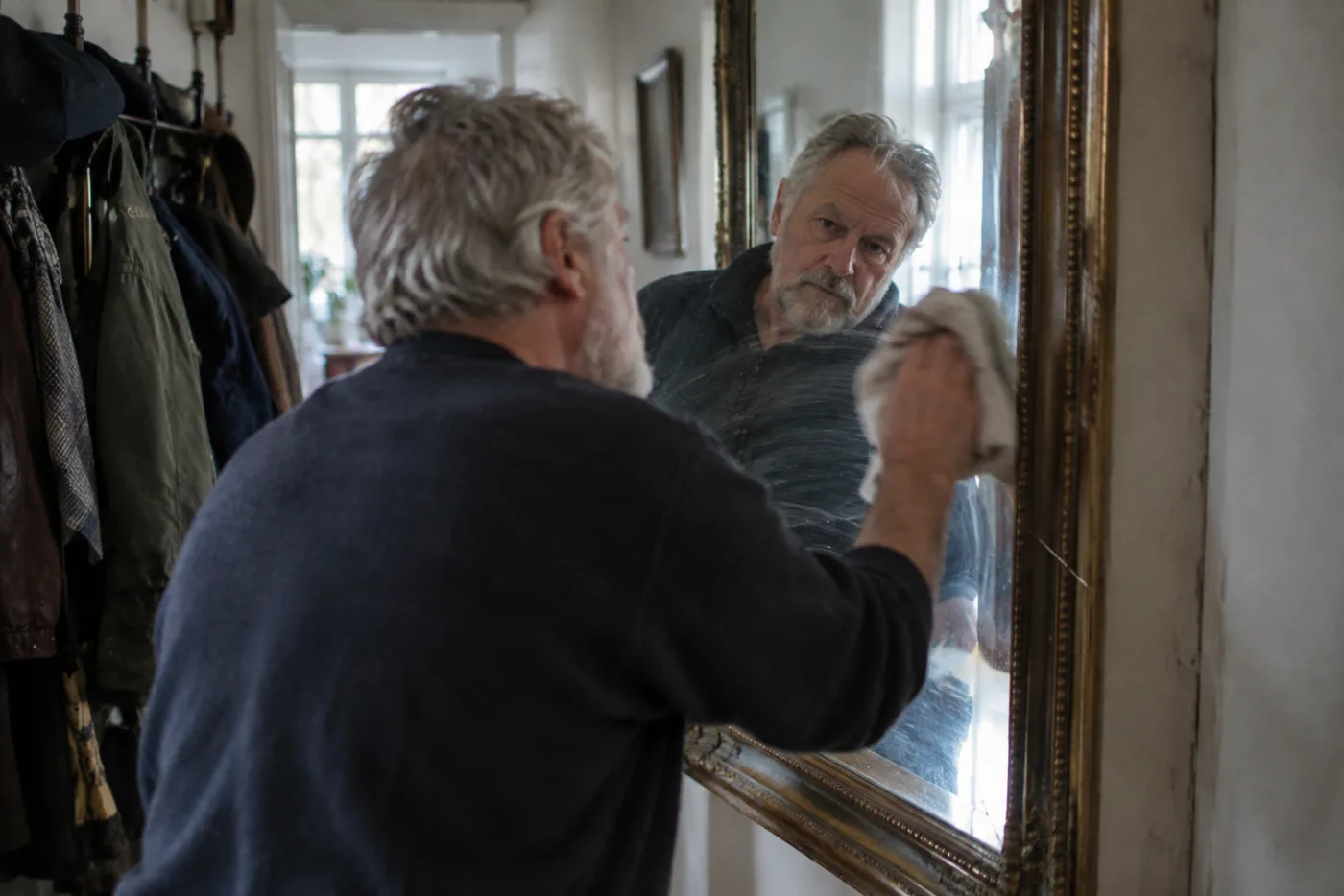 Man polishing a large hallway mirror with a cloth