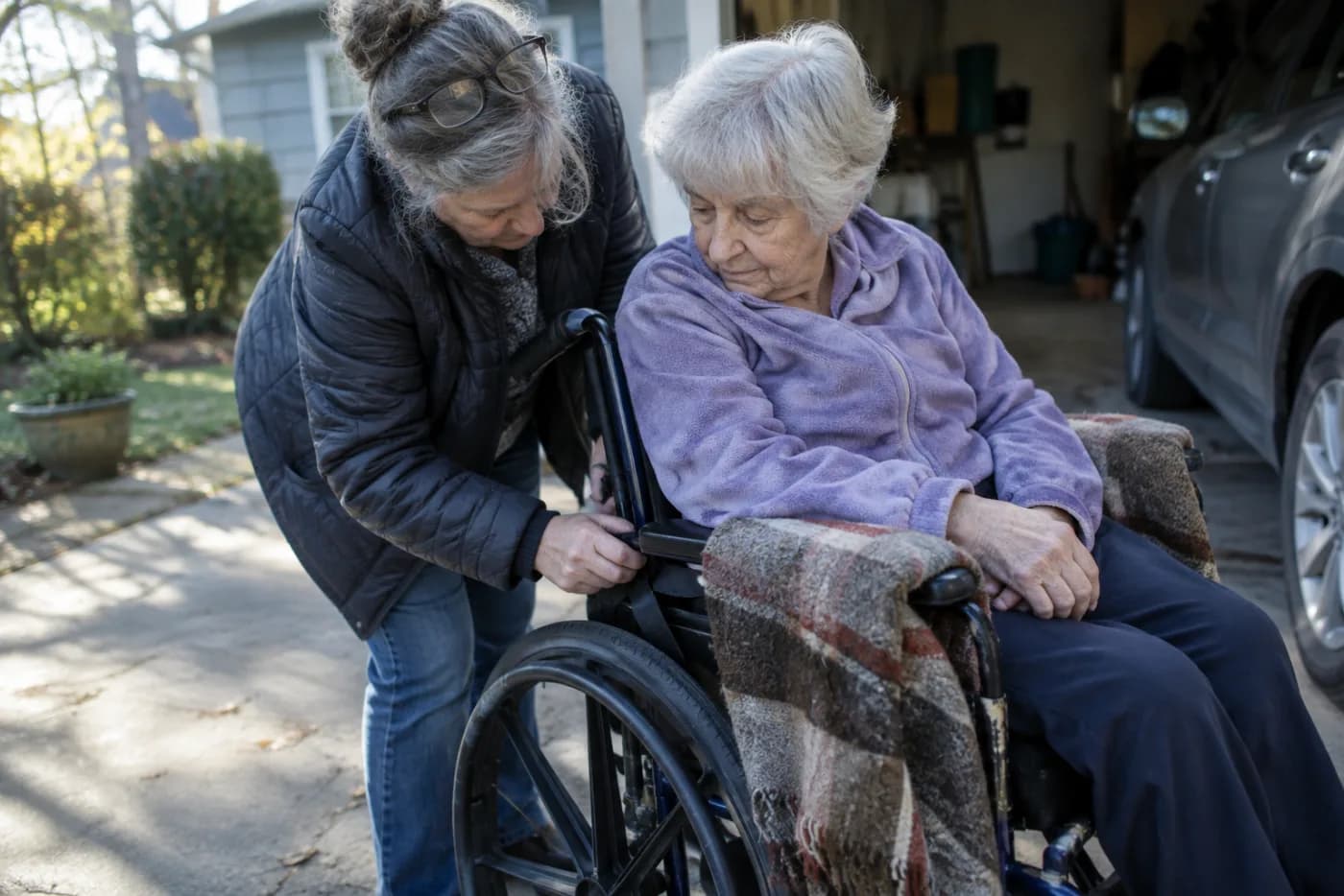 Woman adjusting a wheelchair strap while helping her elderly mother