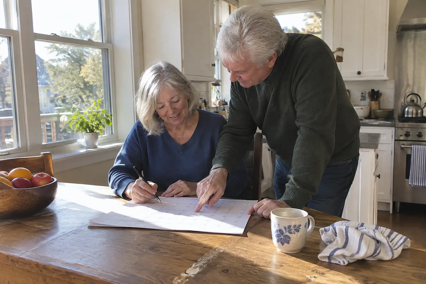 Older woman marking a birthday on a calendar at her kitchen table.
