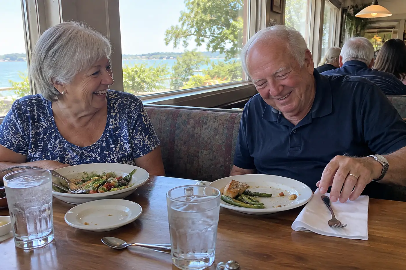 Older woman laughing with a friend over lunch at a restaurant.