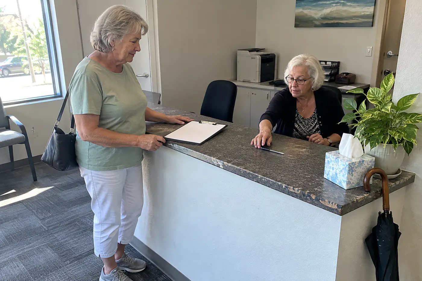 Older woman taking a clipboard at a medical reception desk.