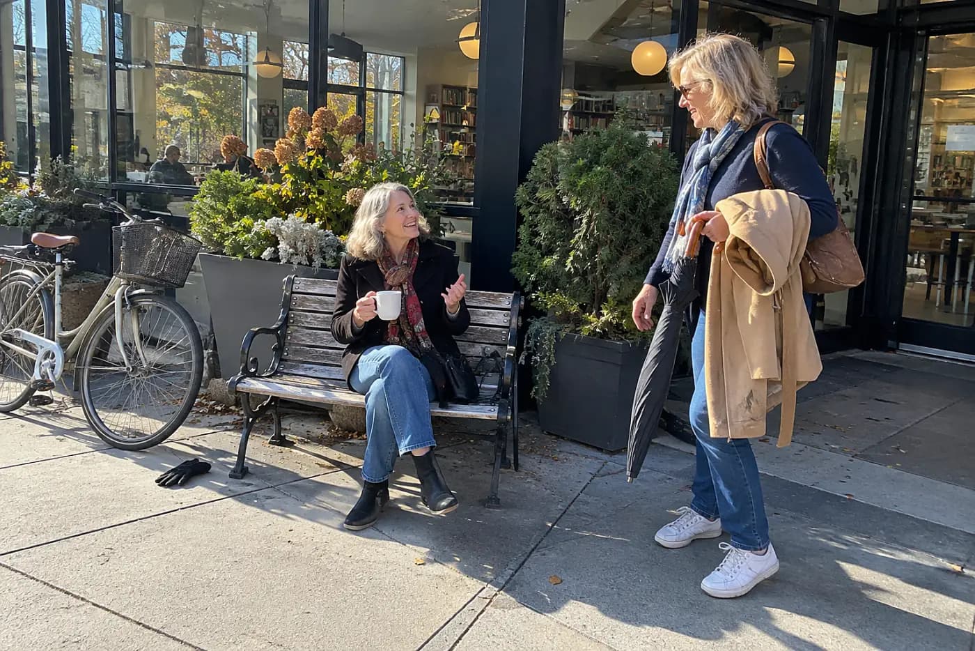 Older woman inviting a friend for coffee outside a library café.
