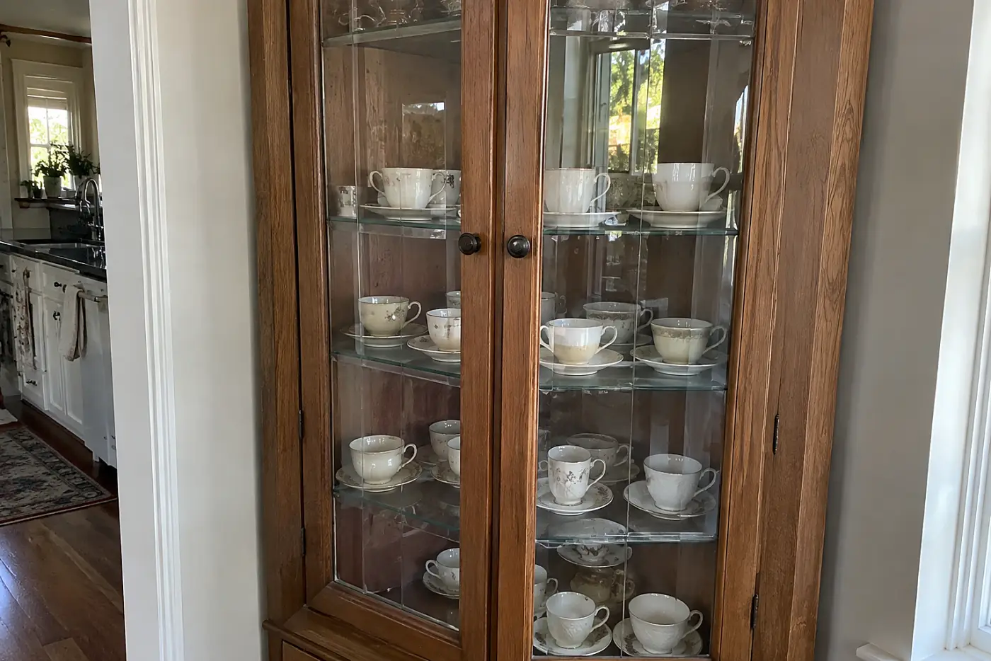 A wooden cabinet displays delicate china teacups and saucers behind glass doors.