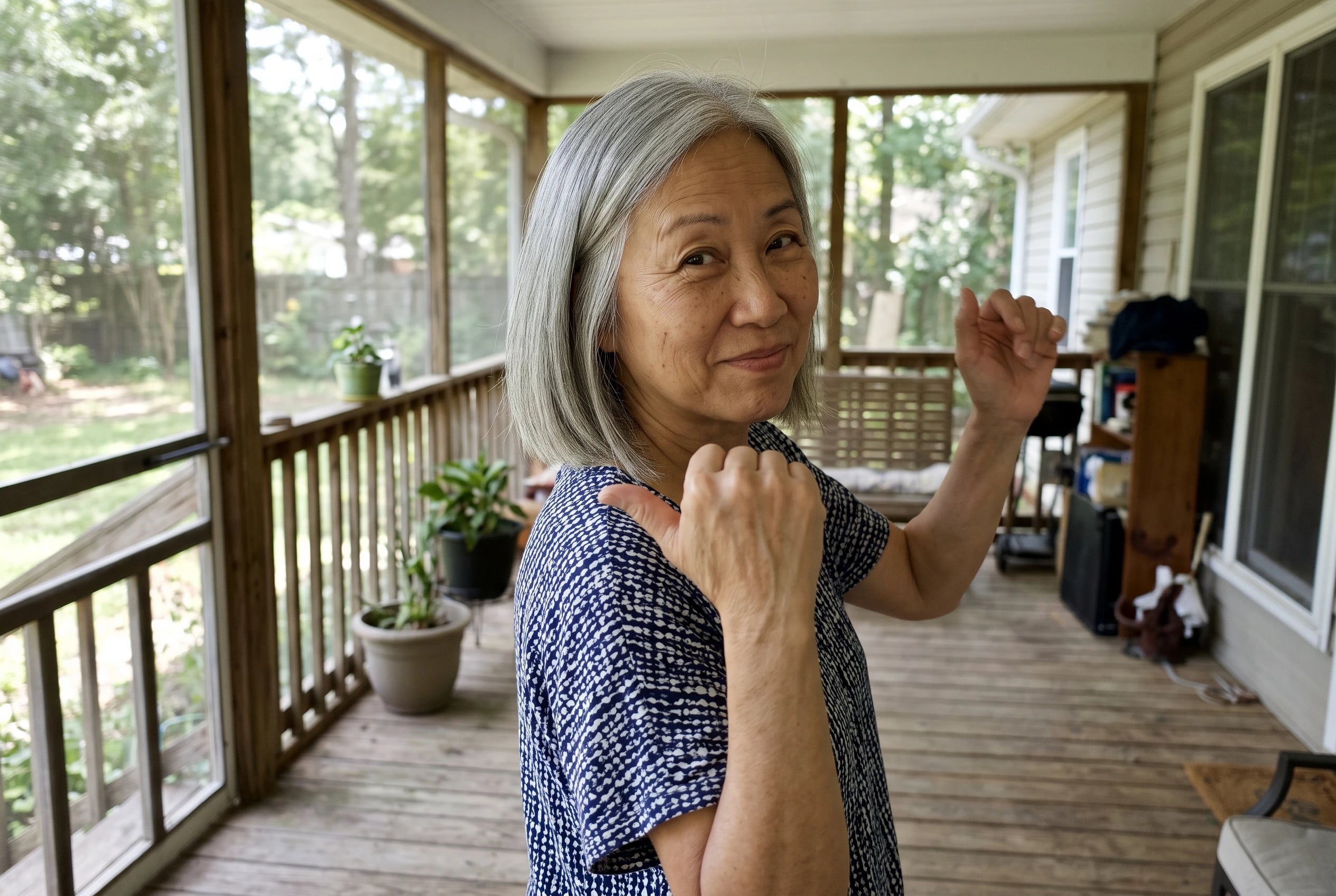 Woman in her sixties flicking her thumb over her shoulder while dancing on a porch.