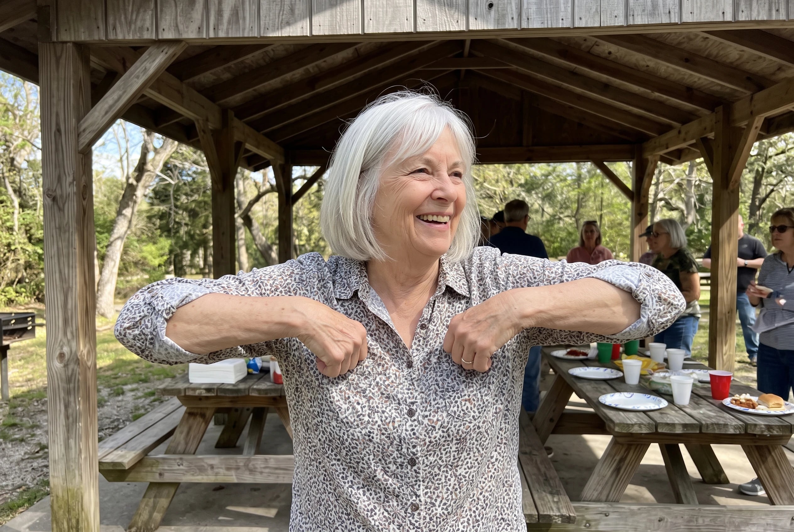 Older woman tucking her elbows into chicken wings while dancing at a picnic.