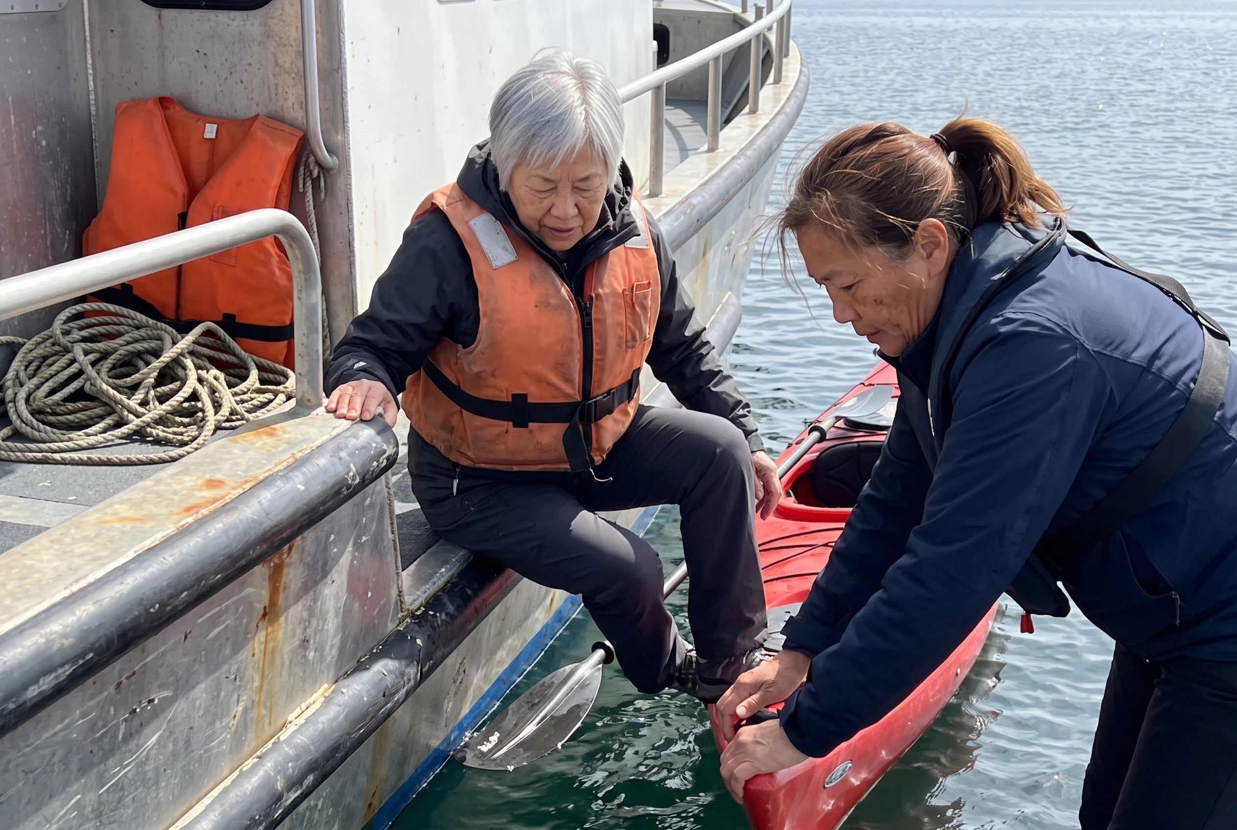 An older woman climbs into a kayak beside a small UnCruise expedition vessel.