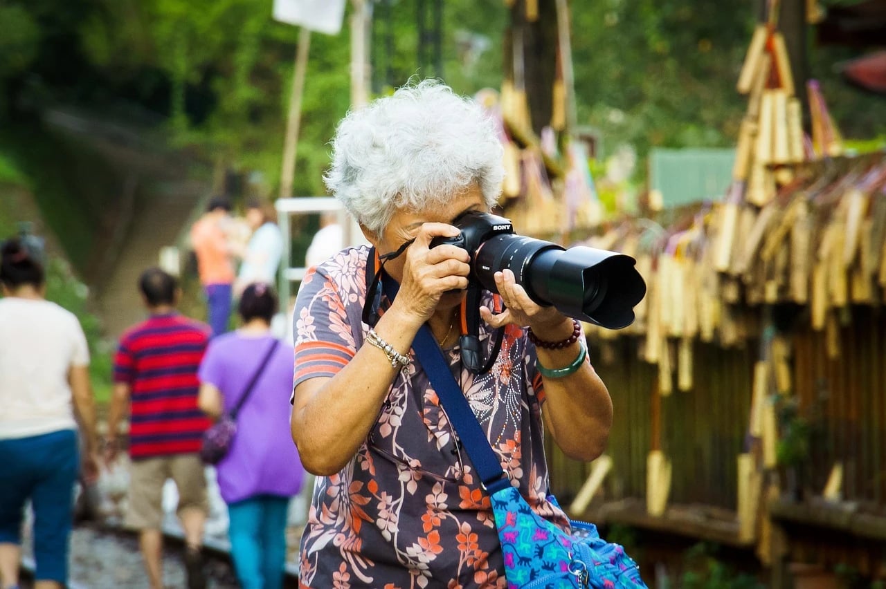 Older woman with short gray hair taking a photo with a large Sony camera outdoors