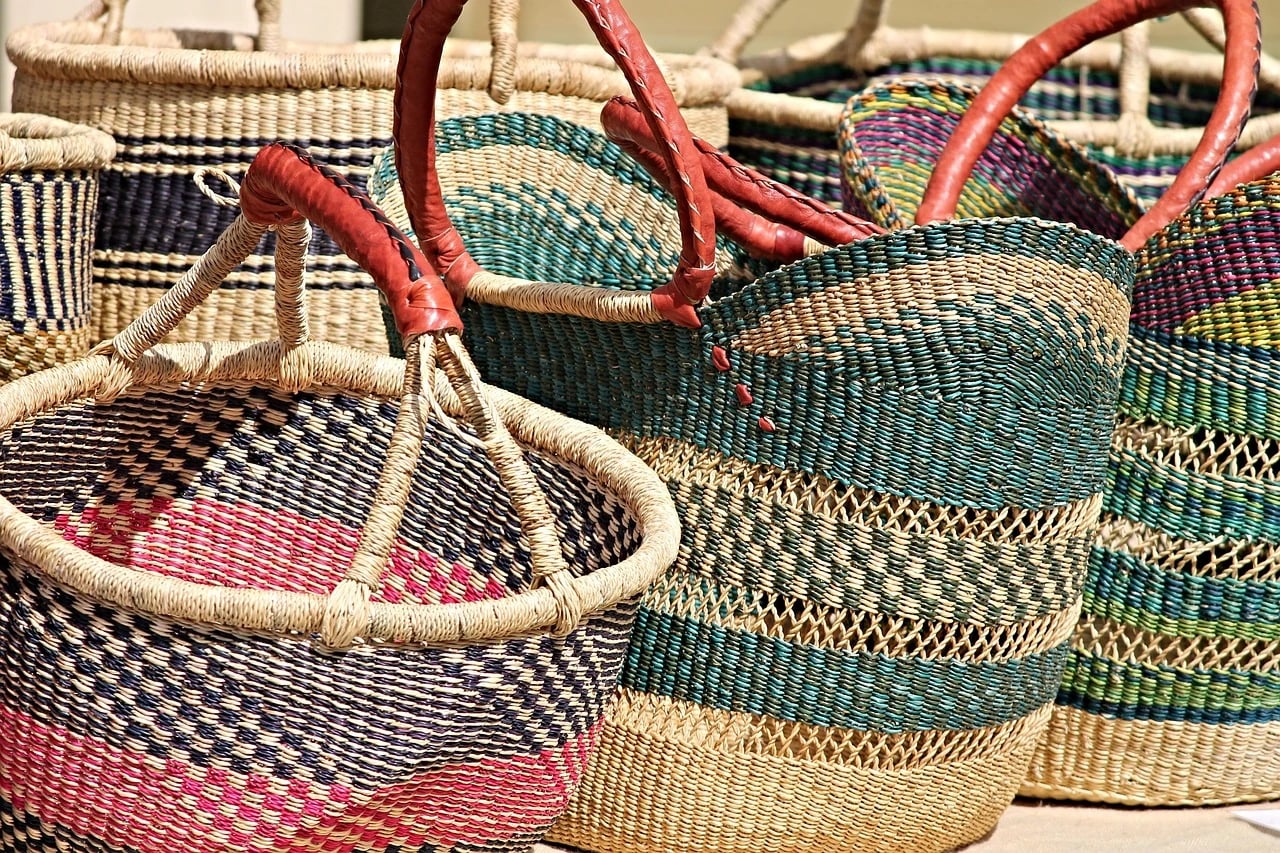 Colorful handwoven straw baskets with leather handles displayed together in sunlight at a market