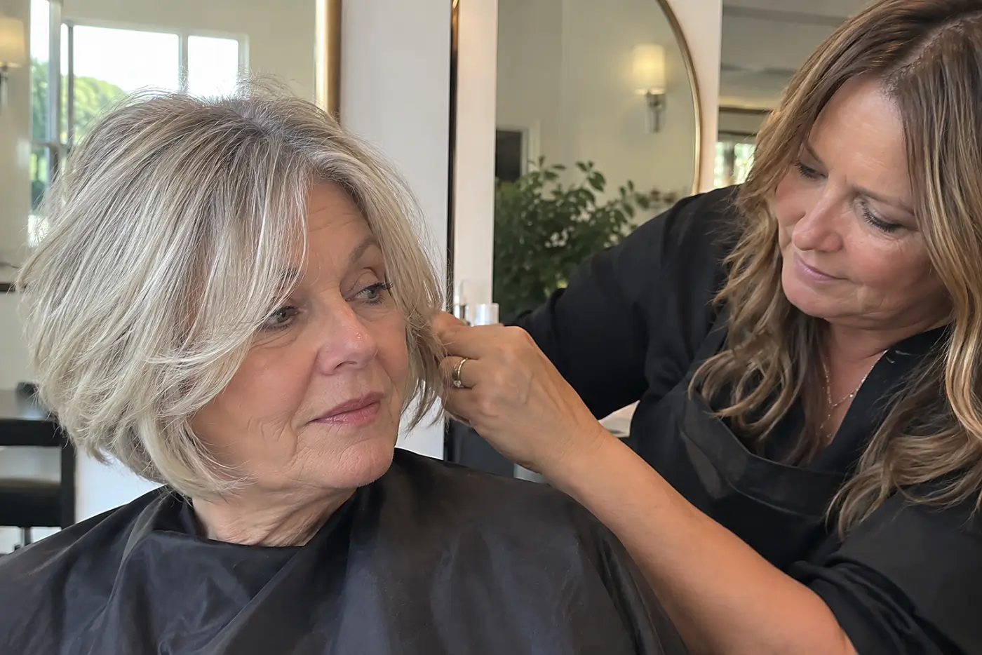 A stylist lifts the ends of a woman’s feathered bob beside a salon mirror.