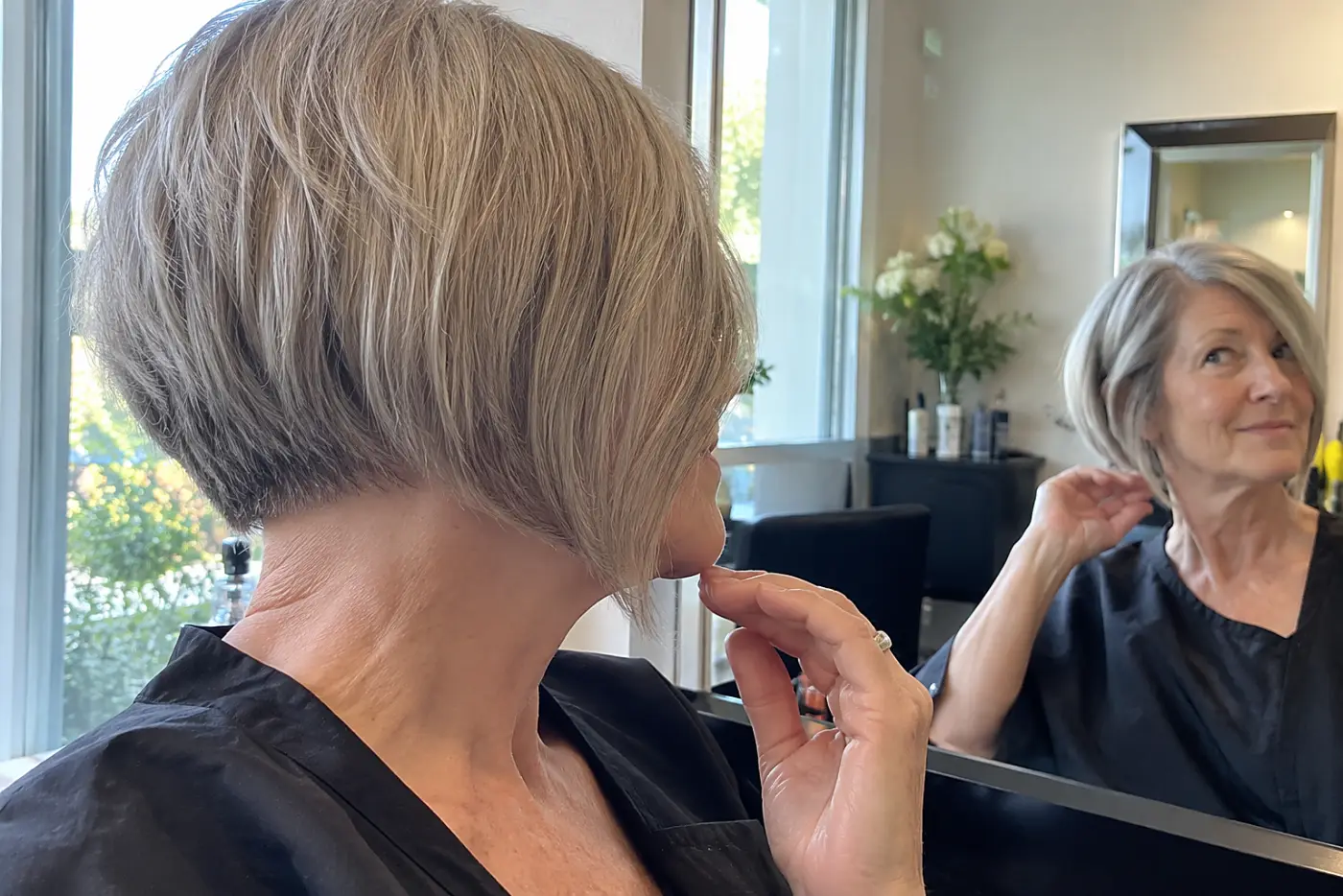 A woman turns sideways to inspect the angled back of her bob at a salon.