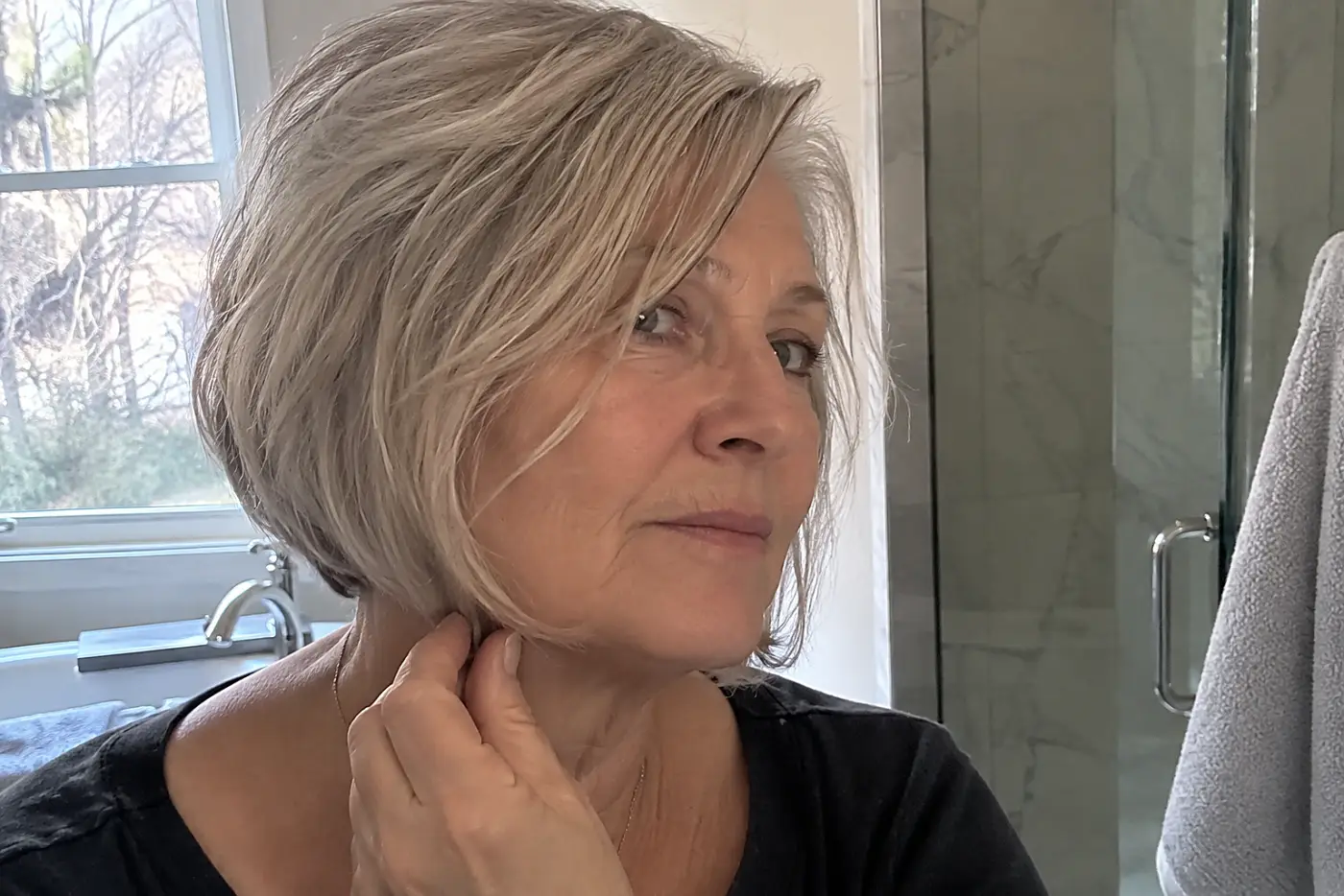 A woman checks the angle of her front hair against her jaw in a bathroom mirror.