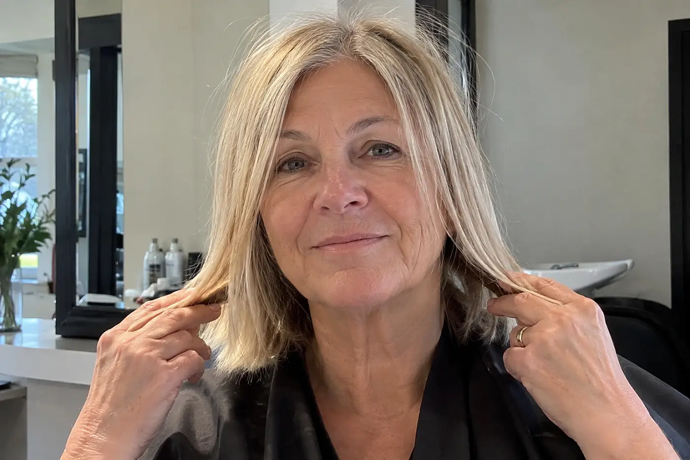 A woman holds her hair at jaw length while facing a salon mirror.